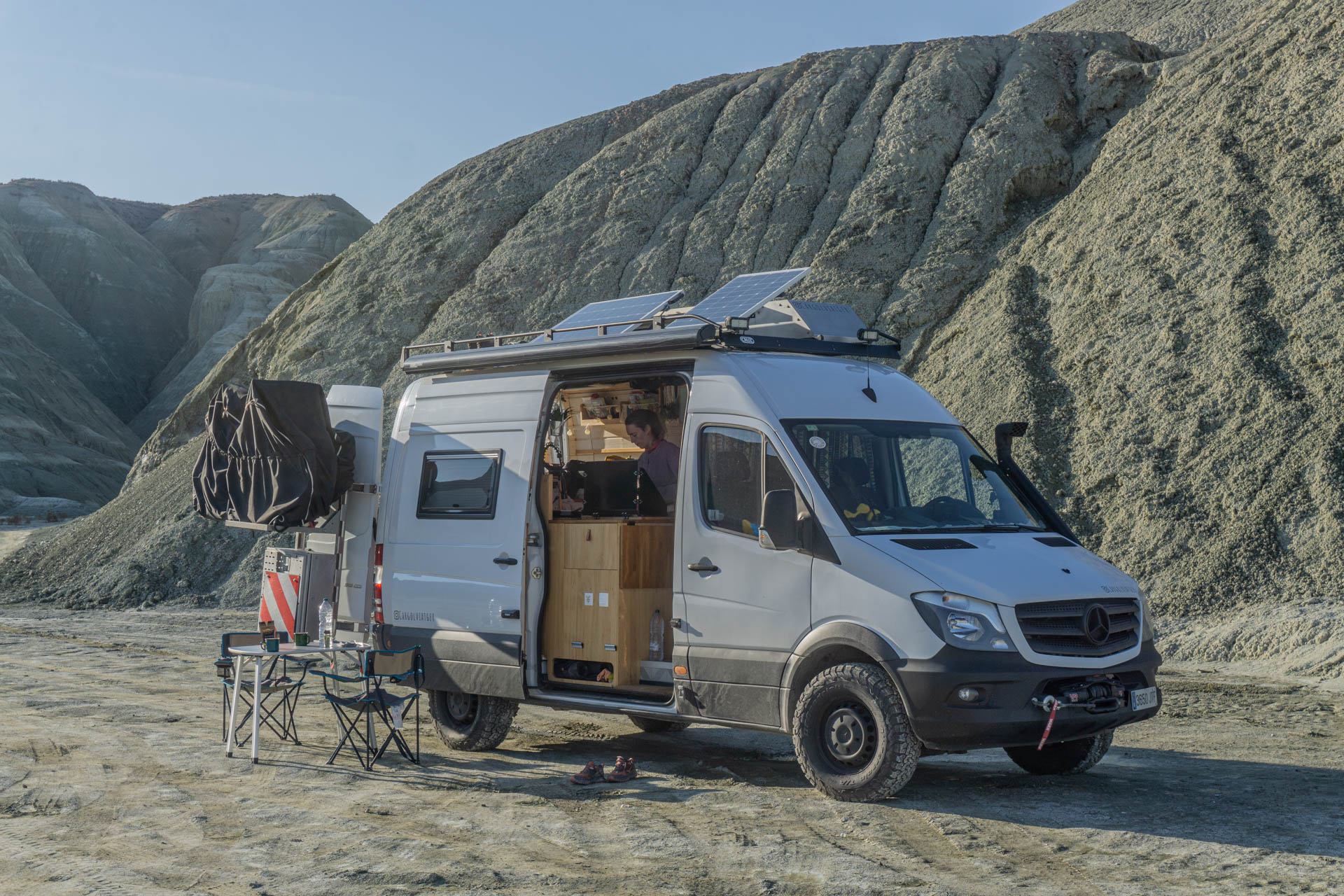 Furgoneta camperitzada de YAK Overland aturada en un terreny erosionat, amb la porta lateral oberta